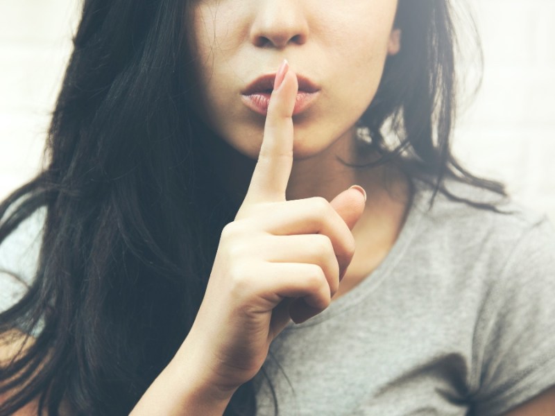 Eine junge Frau hält sich den Zeigefinger vor die Lippen.