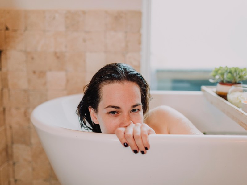 Eine junge Frau liegt in einer Badewanne und schaut über den Wannenrand.