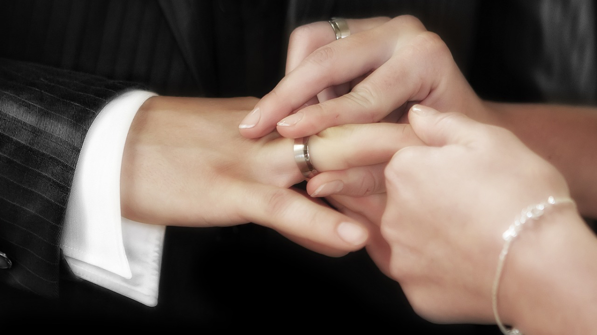 Eine Frau steckt ihrem Mann auf ihrer Hochzeit den Ehering an den Finger.