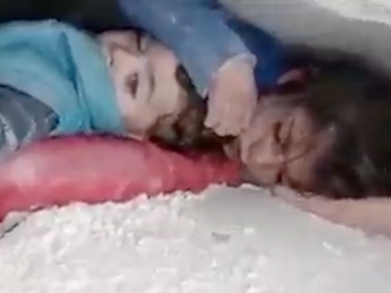 Ein kleines Mädchen wurde unter den Trümmern ihres Hauses in Syrien begraben. Sie schützt den Kopf ihres kleinen Bruders mit der Hand.