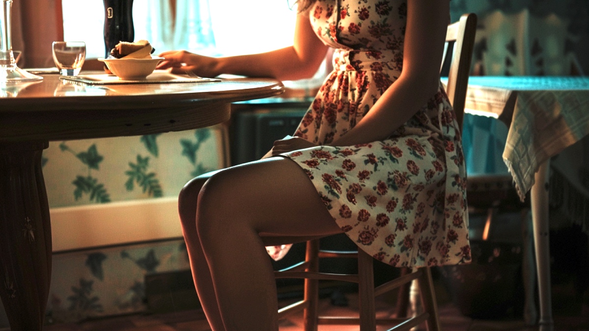 Eine Frau im Sommerkleid am Esstisch.