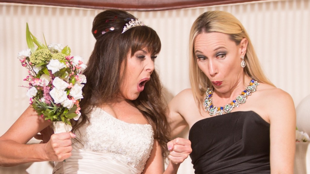 Eine Braut und eine Freundin machen schockierte Gesichter.