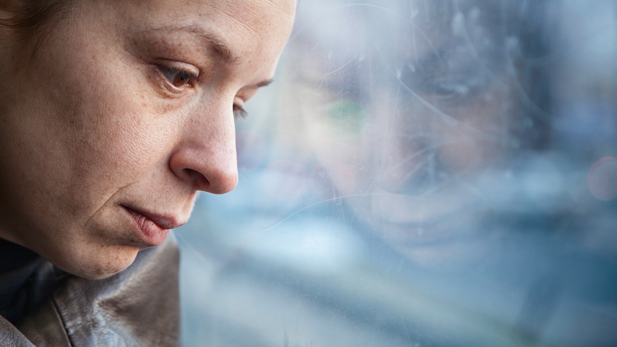 Eine Frau mit traurig-depressivem Gesichtsausdruck lehnt ihren Kopf an eine Scheibe.