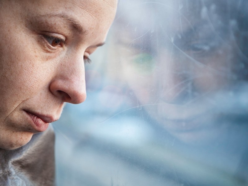 Eine Frau mit traurig-depressivem Gesichtsausdruck lehnt ihren Kopf an eine Scheibe.