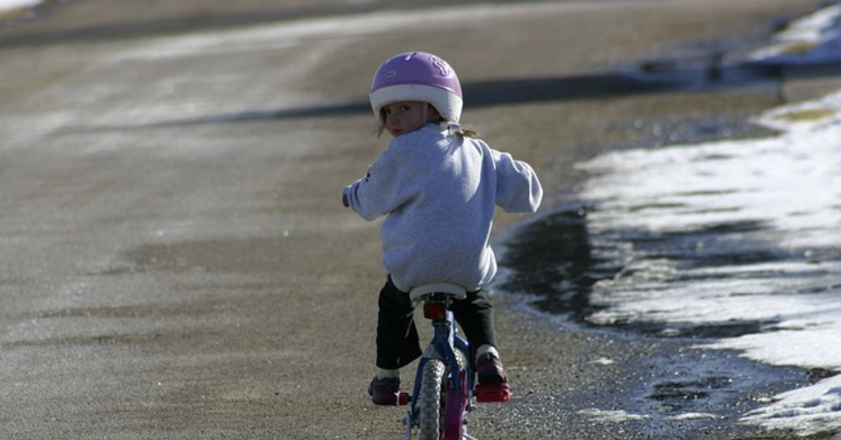 Ein kleines Mädchen mit Helm fährt mit einem Fahrrad.