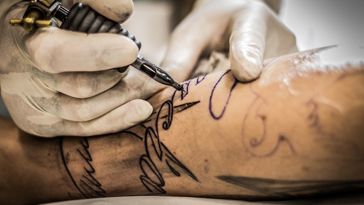 Eine Tätowiernadel sticht ein Tattoo auf den Arm eines Mannes.