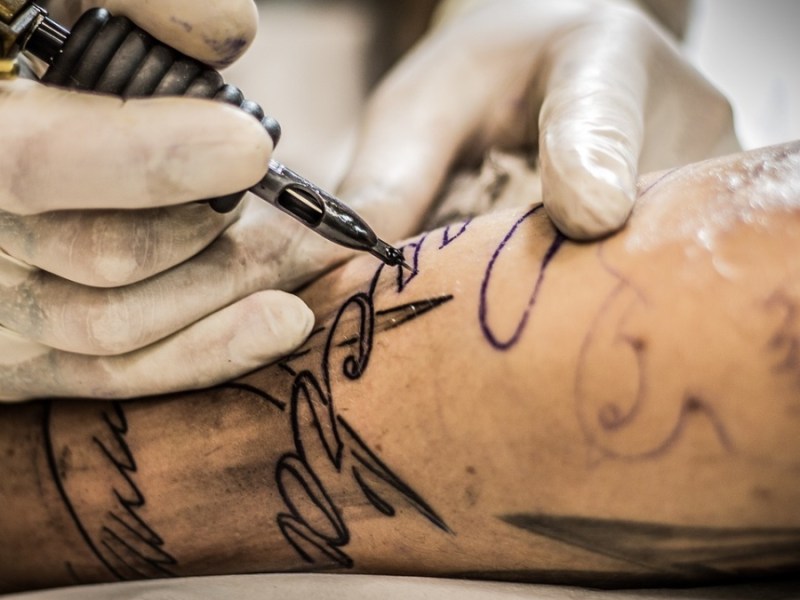 Eine Tätowiernadel sticht ein Tattoo auf den Arm eines Mannes.