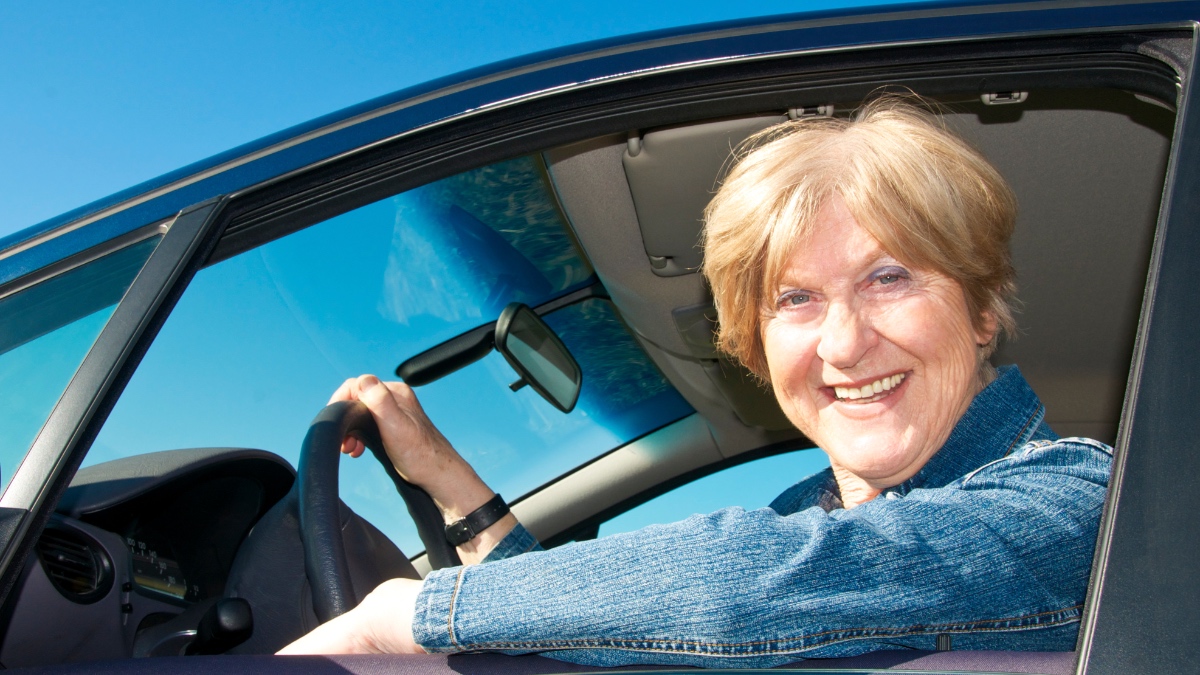 Eine lächelnde ältere Frau sitzt in einem Auto.