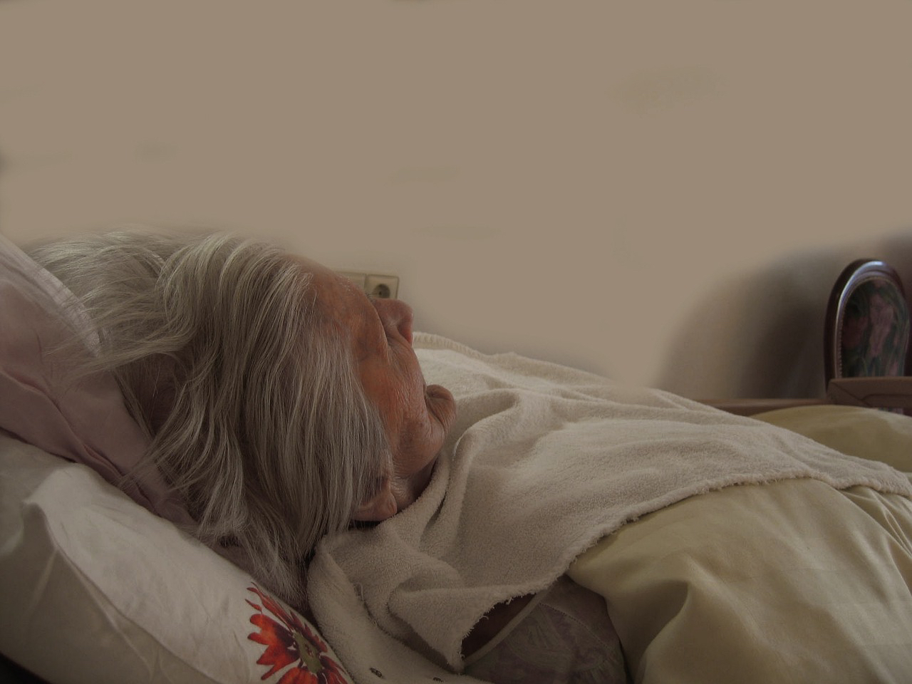 Eine alte, kranke Frau liegt im Seniorenheim im Bett.