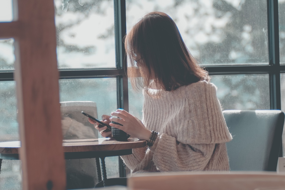 Eine junge Frau sitzt an einem Tisch und blickt auf ihr Smartphone.