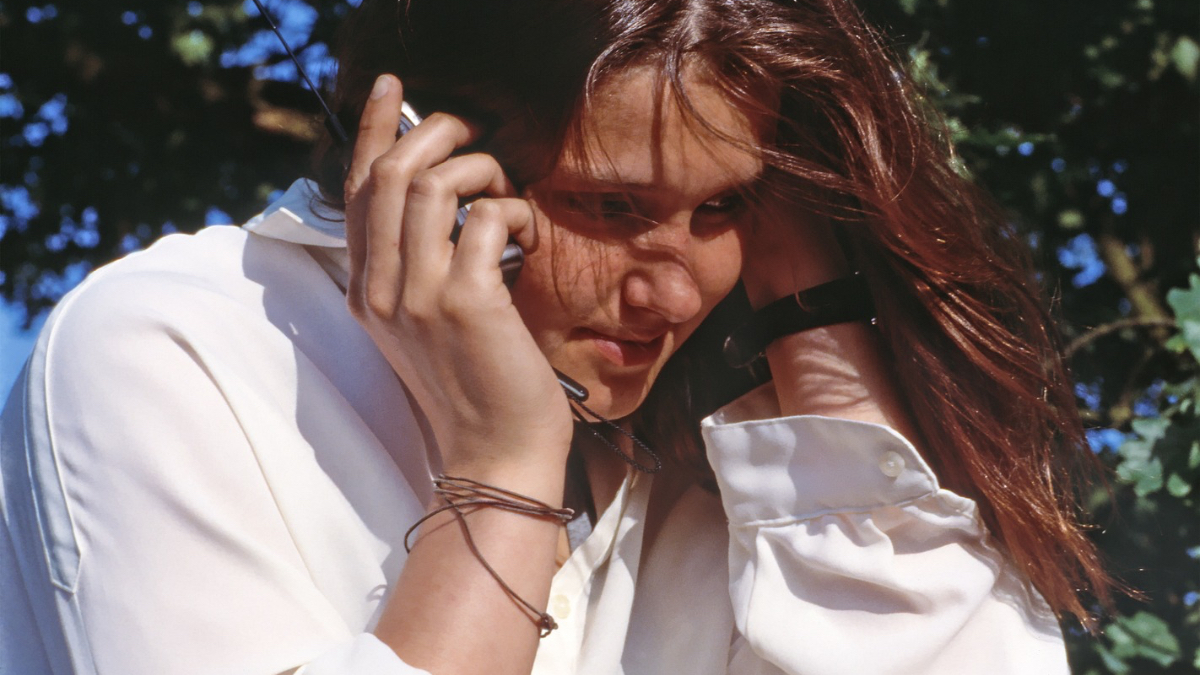 Eine junge Frau mit weißer Bluse telefoniert im Park.
