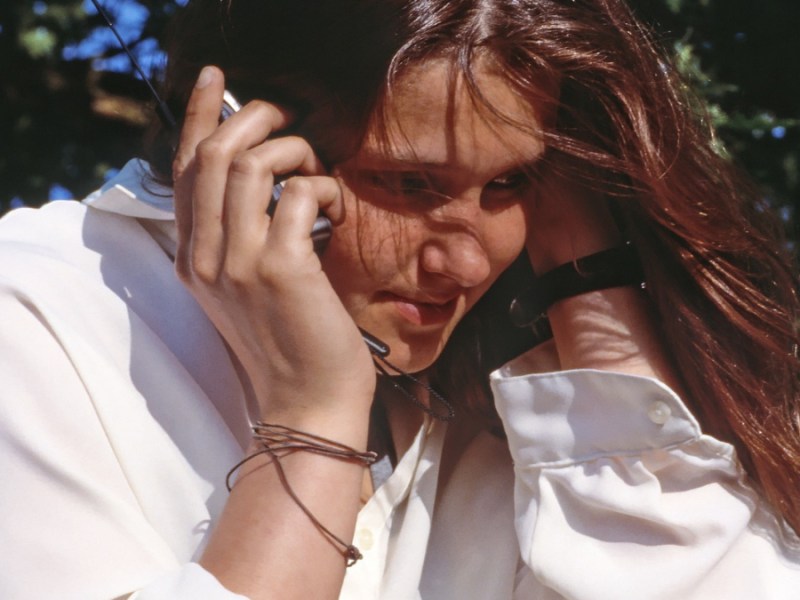 Eine junge Frau mit weißer Bluse telefoniert im Park.
