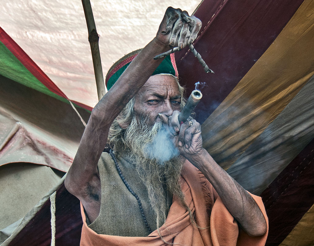 Ein indischer Mönch hebt seinen rechten Arm hoch und raucht Tabak.