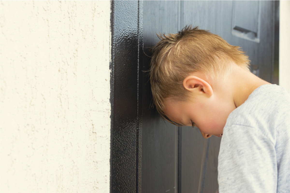 Ein blonder Junge weint und lehnt den Kopf gegen eine Haustür.