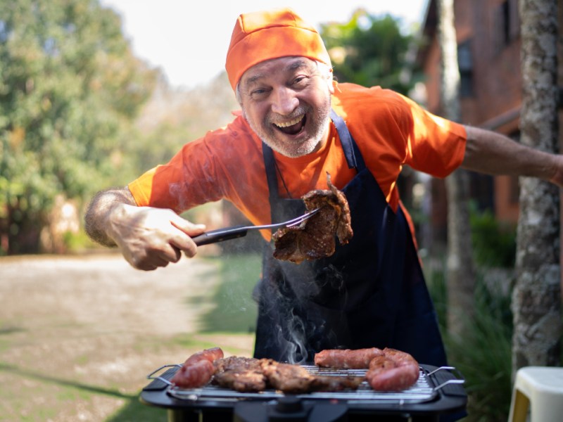 Ein Bild von einem glücklichen Rentner, der Fleisch auf einem Grill zubereitet.