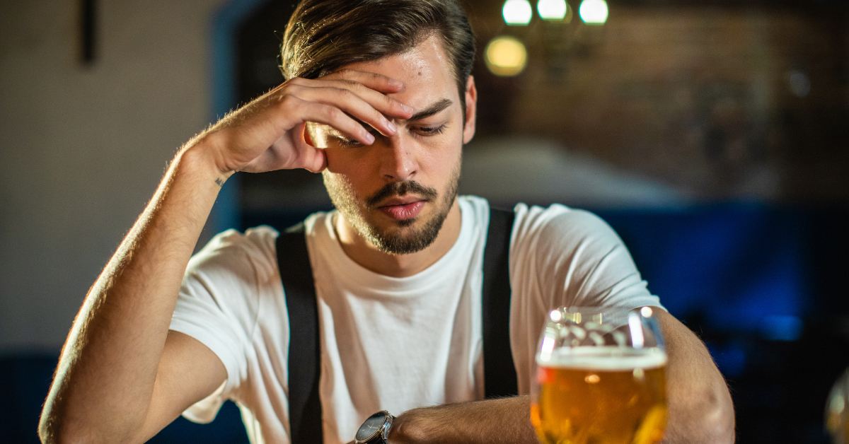 Ein Mann trinkt Bier in einer Kneipe und hält sich den Kopf.