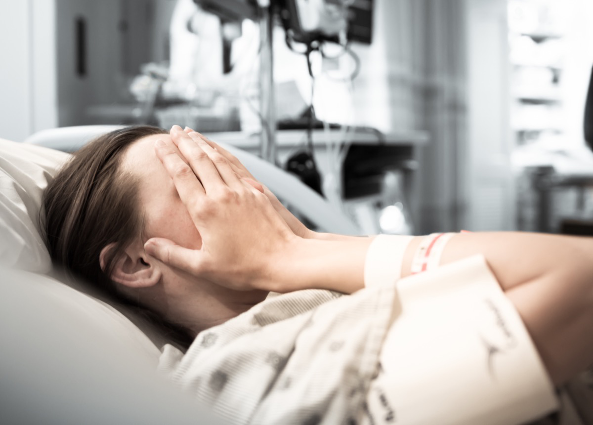 Eine junge Frau liegt in einem Krankenhausbett und hält sich die Hände vors Gesicht.