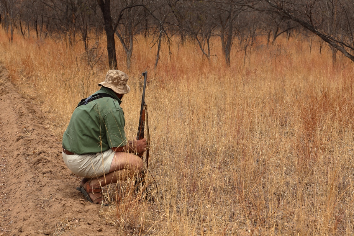 Ein Safari-Führer sitzt mit einem Gewehr in der Hocke.