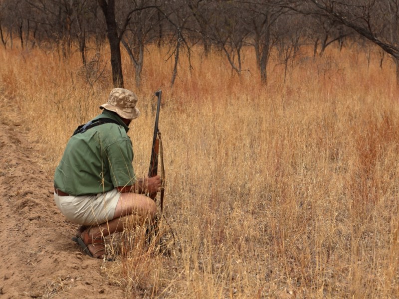 Ein Safari-Führer sitzt mit einem Gewehr in der Hocke.