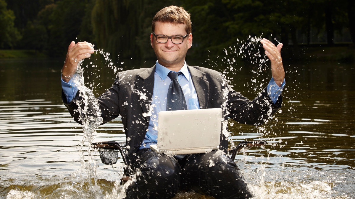 Ein Geschäftsmann sitzt mit Laptop im Wasser.
