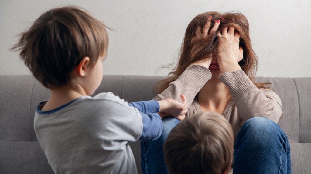 Eine Mutter wird von ihren Kindern genervt und hält sich gestresst die Hände vor das Gesicht.