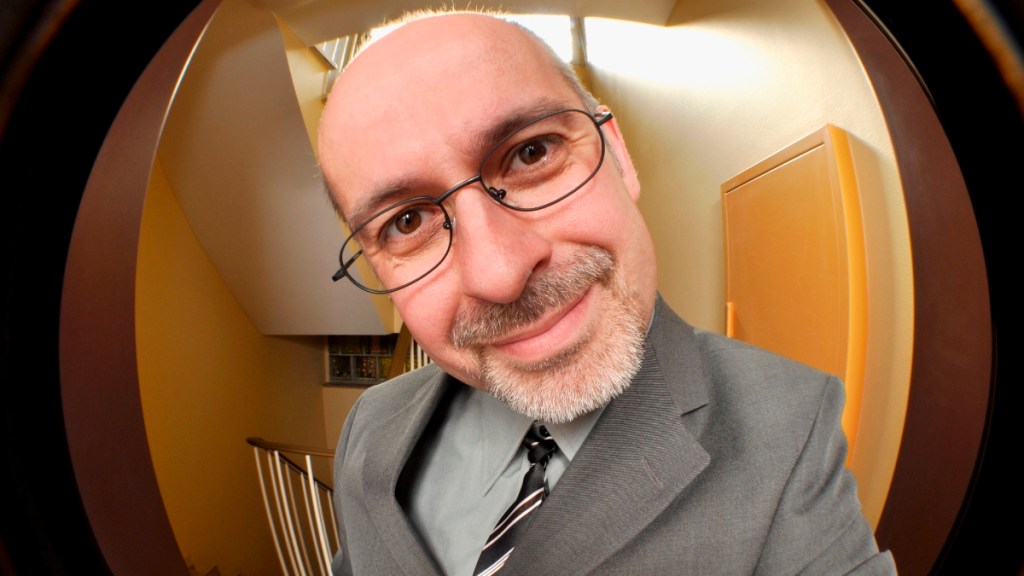 Ein Foto von einem Vertreter in grauem Anzug und Brille durch einen Türspion fotografiert.