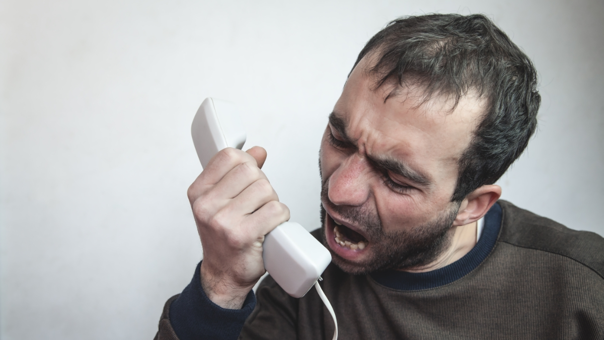 Ein Mann schreit wütend in einen Telefonhörer.