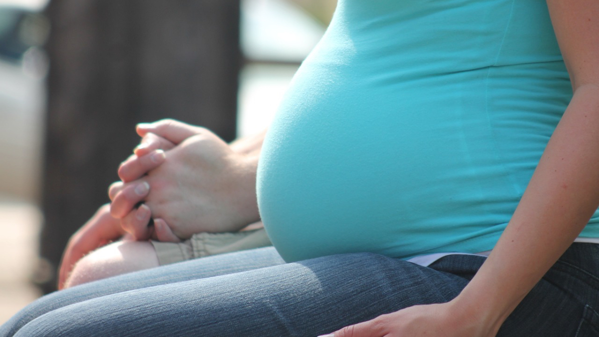 Der Bauch einer schwangeren Frau mit blauem Hemd.