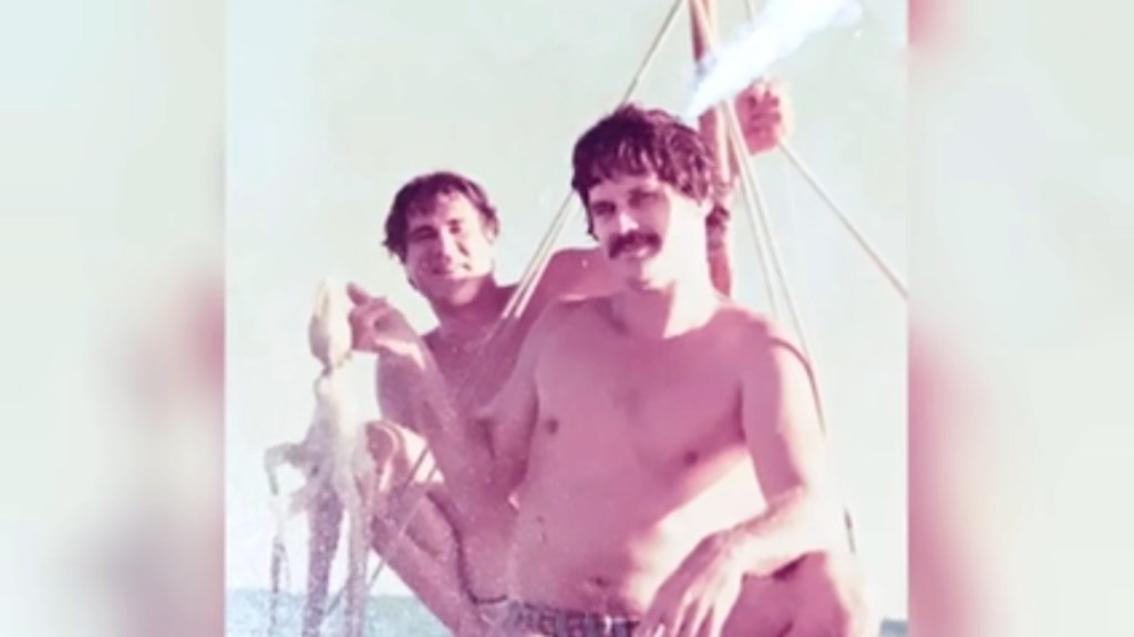 Zwei Männer mit freiem Oberkörper auf einem Boot beim Fischen.
