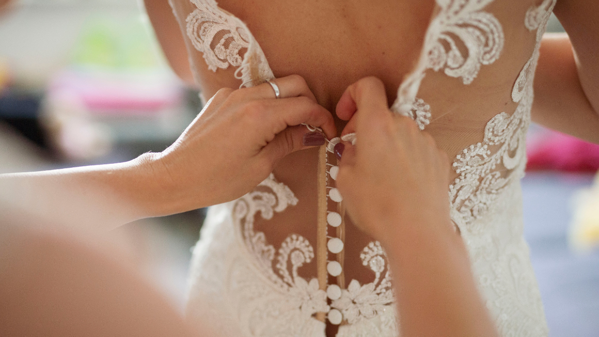Eine Braut bekommt Hilfe beim anziehen ihres Brautkleides.