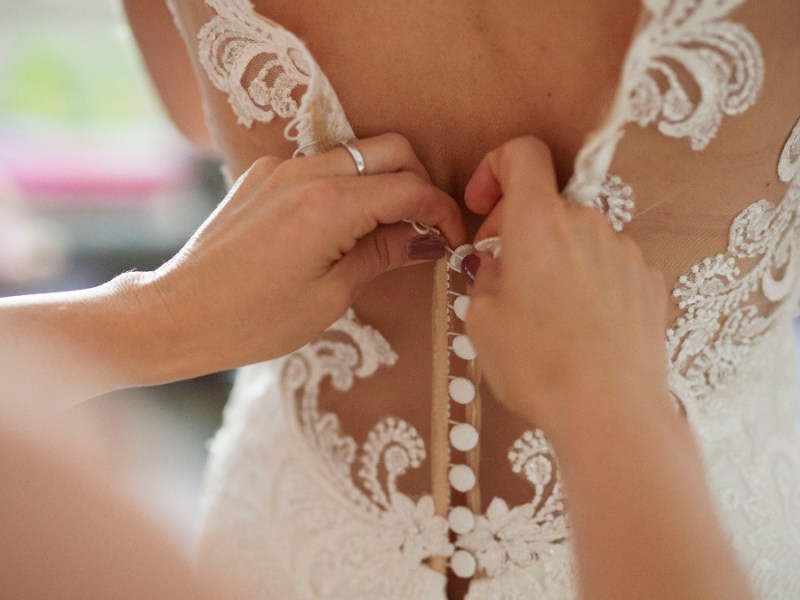 Eine Braut bekommt Hilfe beim anziehen ihres Brautkleides.