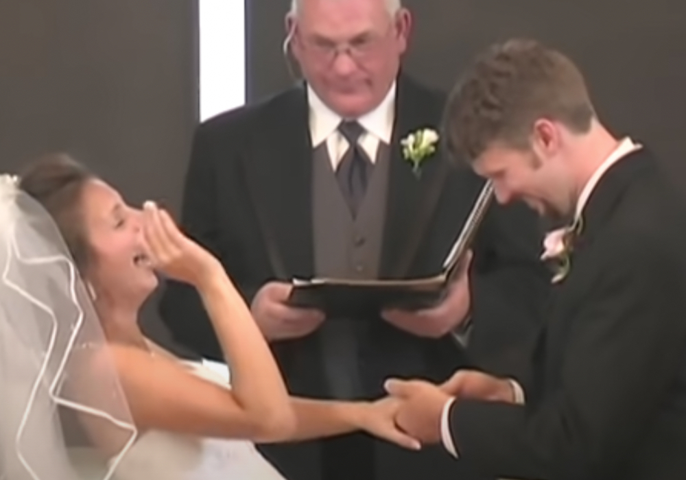 Ein Bräutigam steckt seiner lachenden Braut den Ring an den Finger.