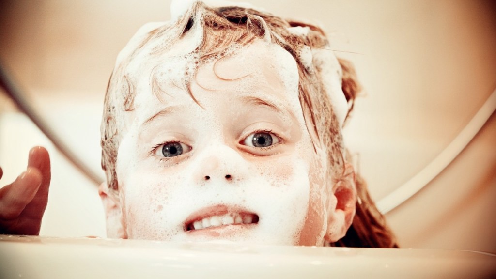 Ein Kind in einer Badewanne mit Schaum im Gesicht.