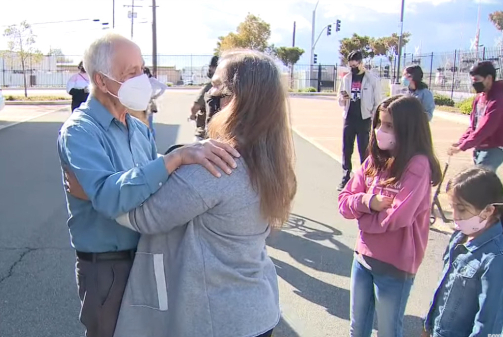 Ein älterer Mann mit Mundschutz und eine Frau umarmen sich auf einem Parkplatz.