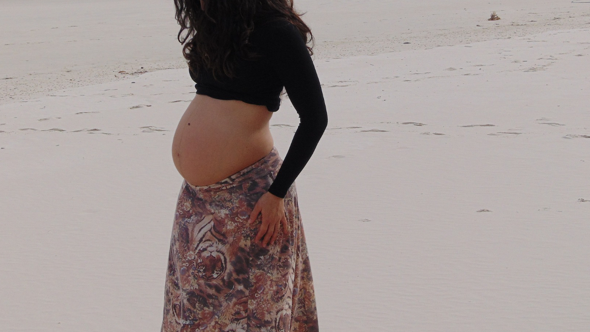 Eine schwangere Frau geht am Strand spazieren.