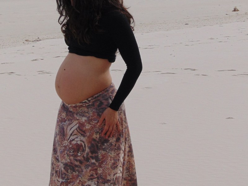 Eine schwangere Frau geht am Strand spazieren.