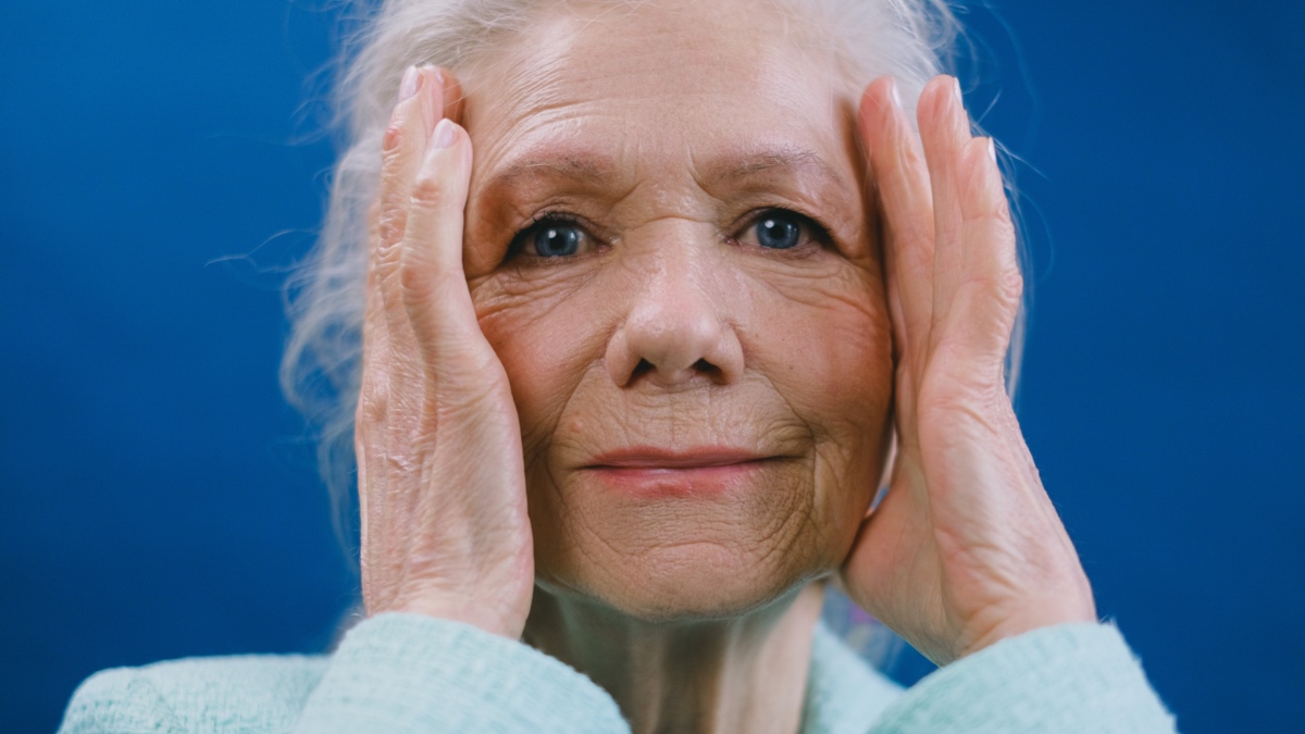 Eine ältere Frau fasst sich an den Kopf.