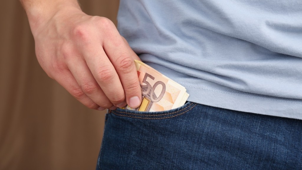 Mann steckt Geld in die Tasche einer Jeans, Nahaufnahme.