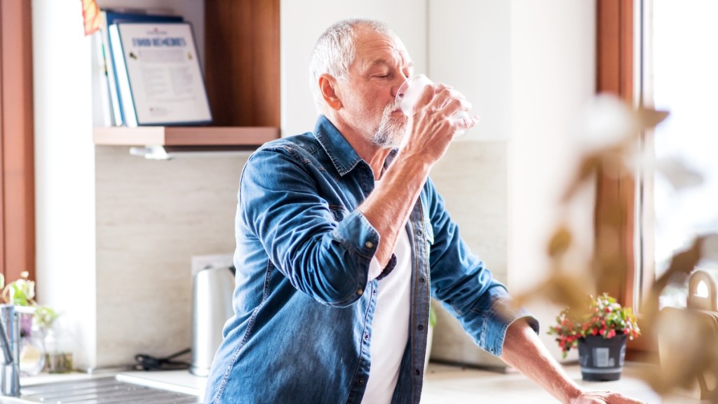 Ein älterer Mann trinkt Wasser in der Küche.