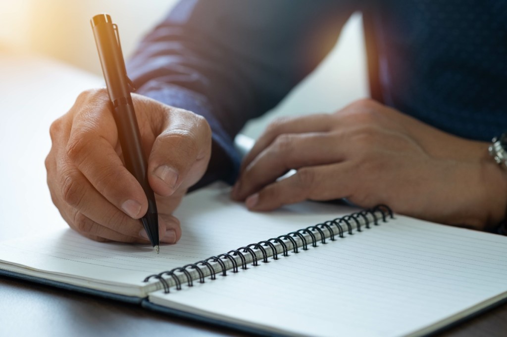 Nahaufnahme von Mann mit Stift und Tagebuch auf Schreibtisch.