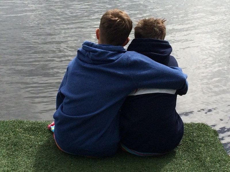 Zwei Brüder sitzen auf einem Steg am Wasser und umarmen sich.
