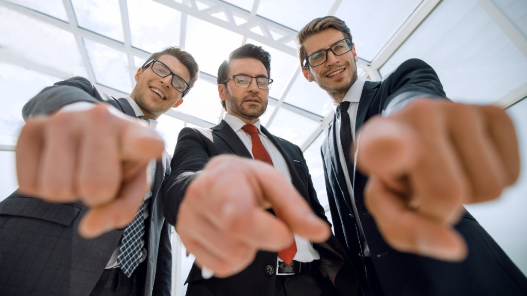 Drei Geschäftsmänner zeigen mit dem Zeigefinger in die Kamera.