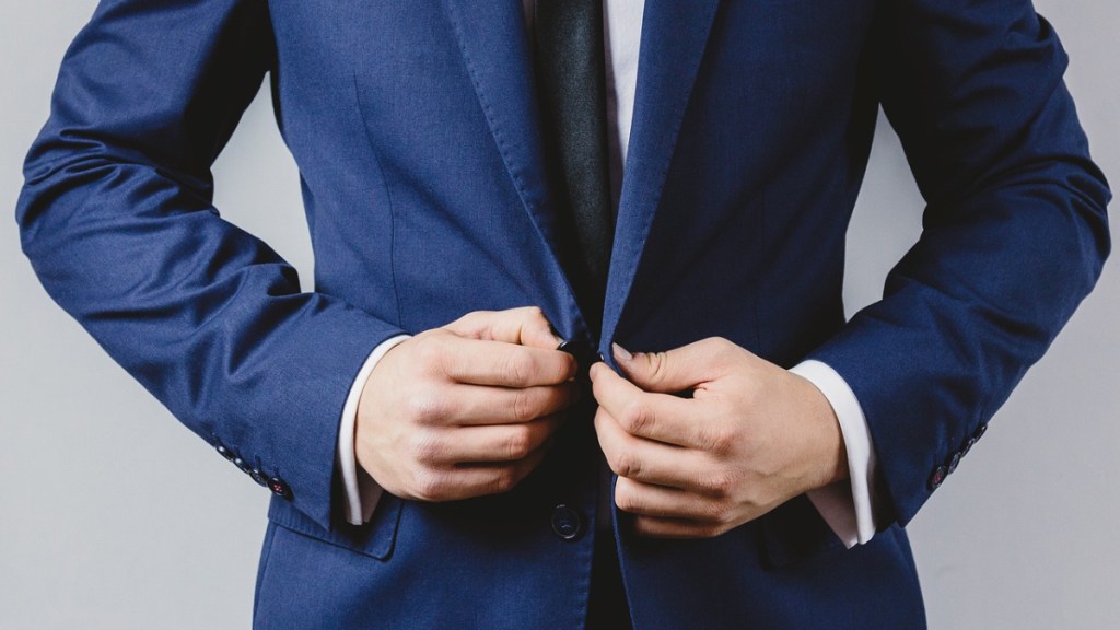 Ein Geschäftsmann in einem blauen Anzug knöpft sich das Jackett zu.