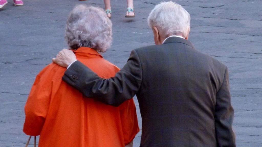 Ein alter Mann legt beim Spazieren den Arm um seine Frau.
