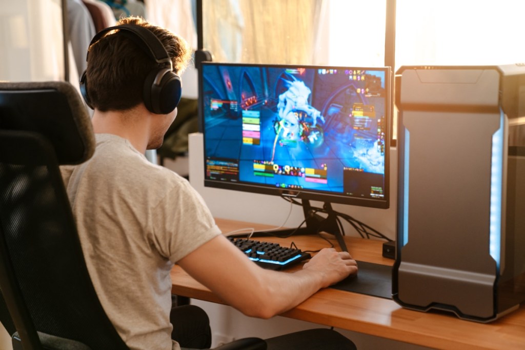 Brünetter Mann mit Kopfhörern spielt ein Videospiel auf seinem Computer.