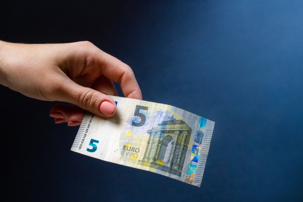 Eine Hand hält eine Fünf-Euro-Banknote.
