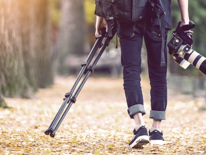 Professioneller Fotograf mit Kamera und Stativ im Herbst.