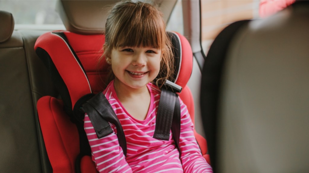 Lächelndes Mädchen mit Sicherheitsgurt auf dem Rücksitz.