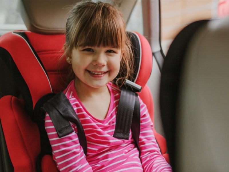 Lächelndes Mädchen mit Sicherheitsgurt auf dem Rücksitz.