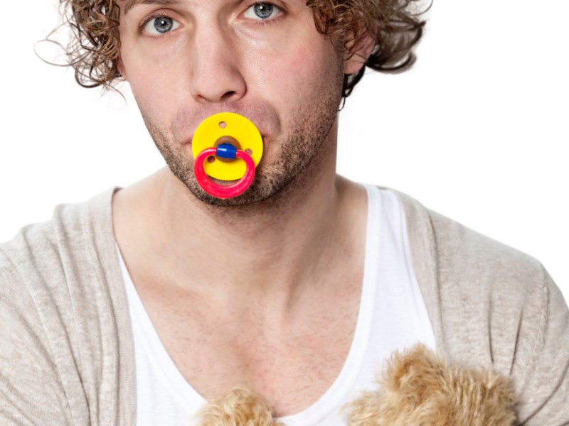 Ein junger Mann mit Schnuller im Mund und Teddybär im Arm.